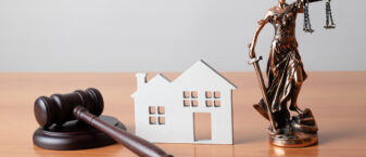 marteau de la justice, maison en carton et guerrière maintenant la balance de la justice dans les mains sous forme de statuette en bois, le tout posé sur un bureau