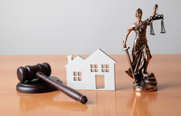 marteau de la justice, maison en carton et guerrière maintenant la balance de la justice dans les mains sous forme de statuette en bois, le tout posé sur un bureau - Agrandir l'image, fenêtre modale