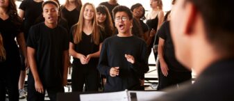 Des adolescents et jeunes adultes de noir vêtus chantent en choeur devant leur professeur