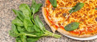 une pizza dans une assiette servie sur un comptoir, avec une part découpée, et un bouquet de basilique posé à côté de l'assiette.