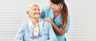 une infirmière souriante parle avec une personne âgée assise sur une chaise