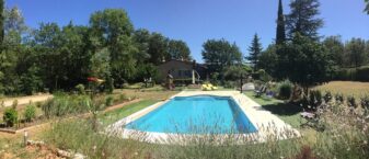 grande piscine dans décor de garrigue avec maison en fond