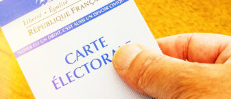 photo d'une carte électorale tenue à la main sur fond jaune