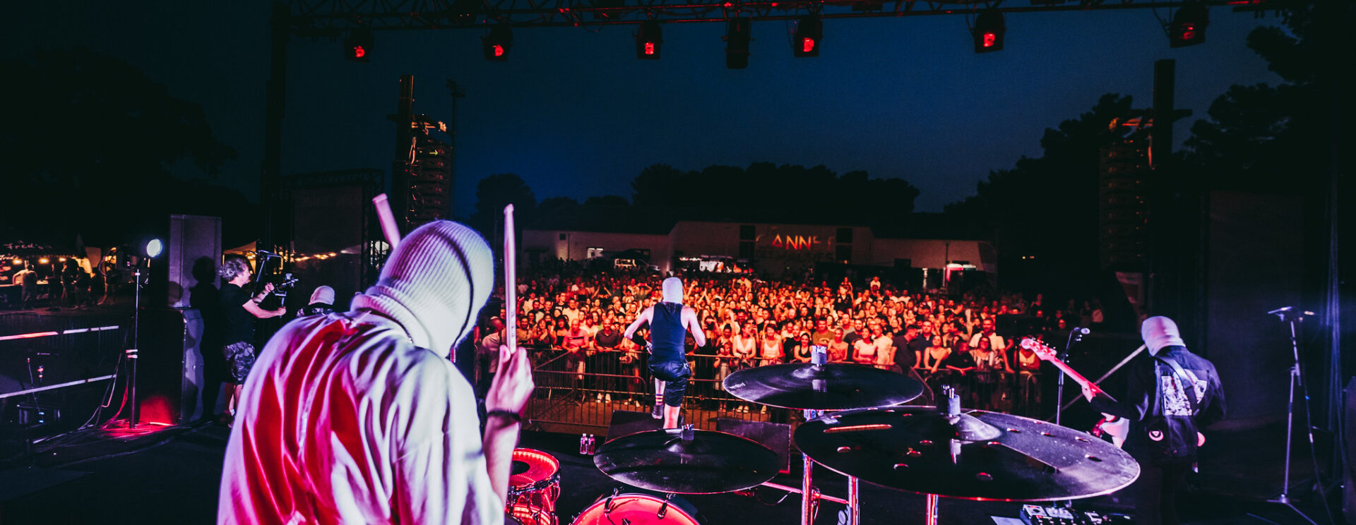 un groupe de rock cagoulé fait face à son public dans la pénombre de la nuit