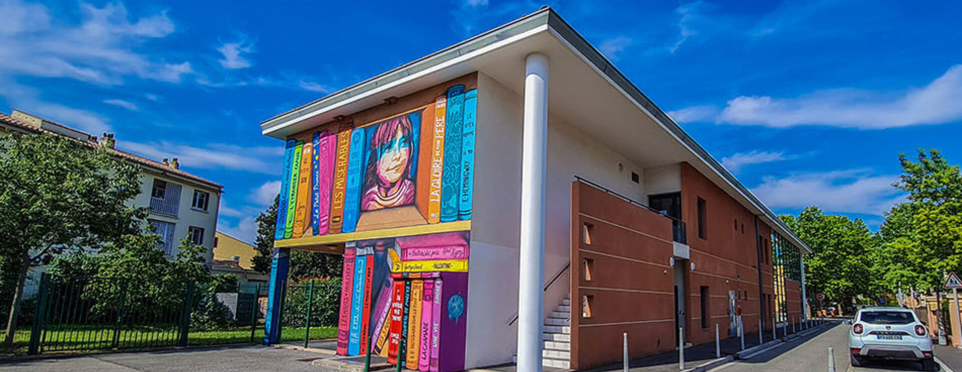 fronton de bâtiment couleur ocre avec grandes baie vitrées et une fresque en premier plan