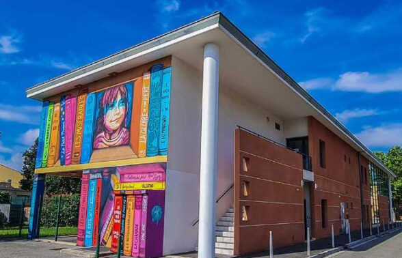batiment coueur blanc et ocre avec une fresque de livres peinte dessus très colorée - Agrandir l'image, fenêtre modale