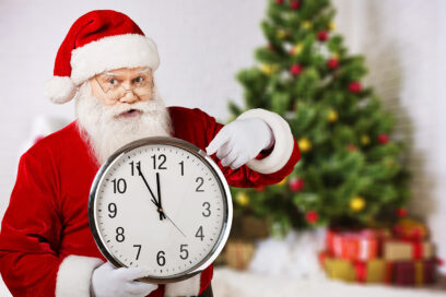 un père noël montre une horloge, un sapin et des cadeaux derrière lui. - Agrandir l'image, fenêtre modale