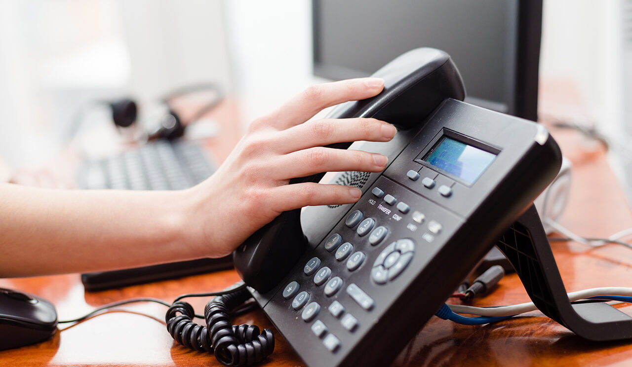 une main posée sur un téléphone fixe de bureau, prête à décrocher le combiné