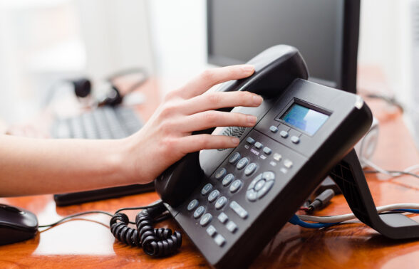 une main posée sur un téléphone fixe de bureau, prête à décrocher le combiné - Agrandir l'image, fenêtre modale